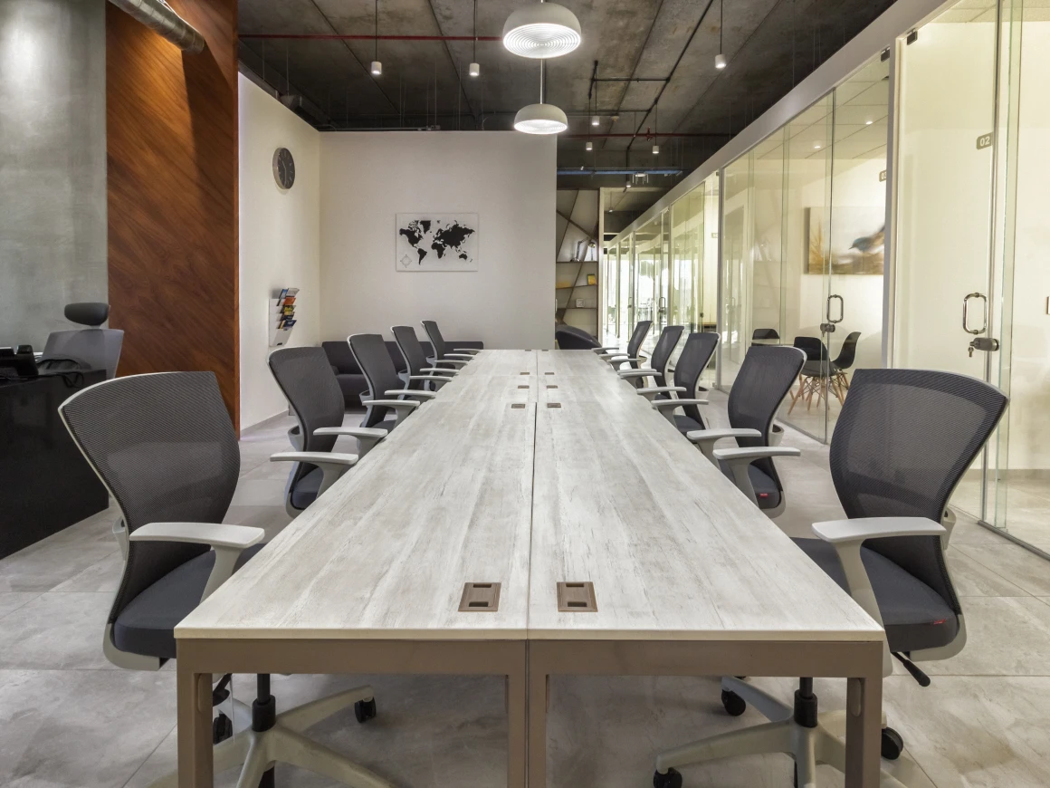 Mesa de juntas larga de madera clara con sillas grises, vista desde un extremo, en oficina de diseño industrial