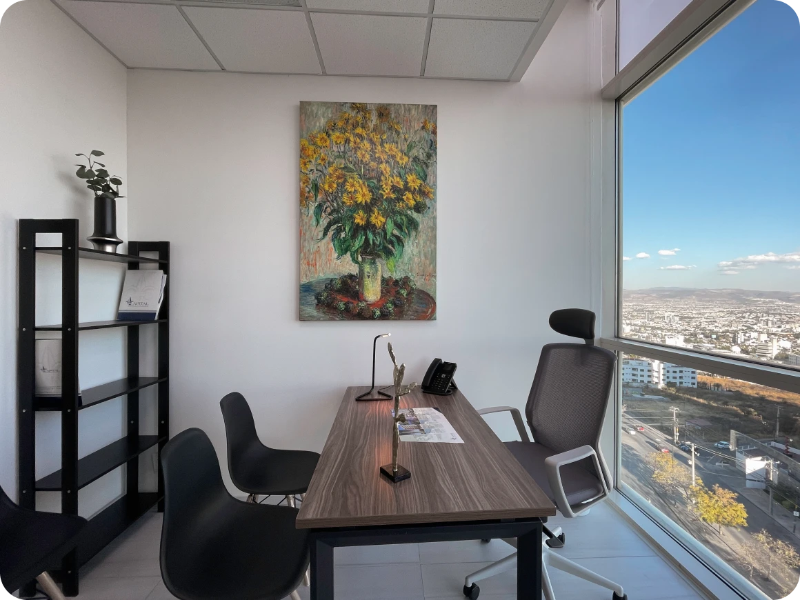 Oficina privada con escritorio de madera, sillas negras, cuadro de flores en la pared y vista a la ciudad