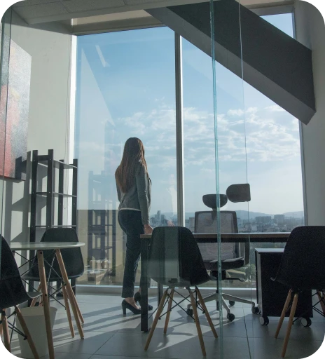 Mujer de pie observando la ciudad a través de un amplio ventanal en una oficina